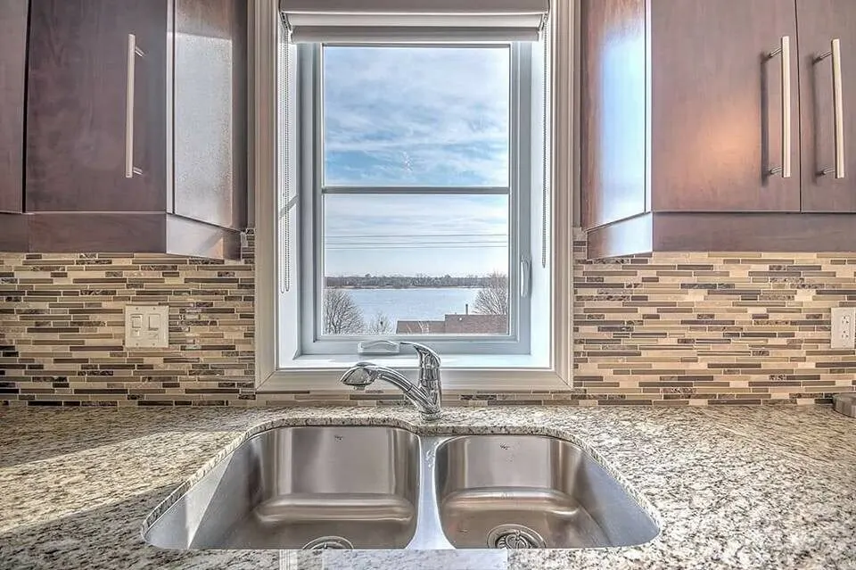 Double sink under a window with granite counters and a mosaic backsplash